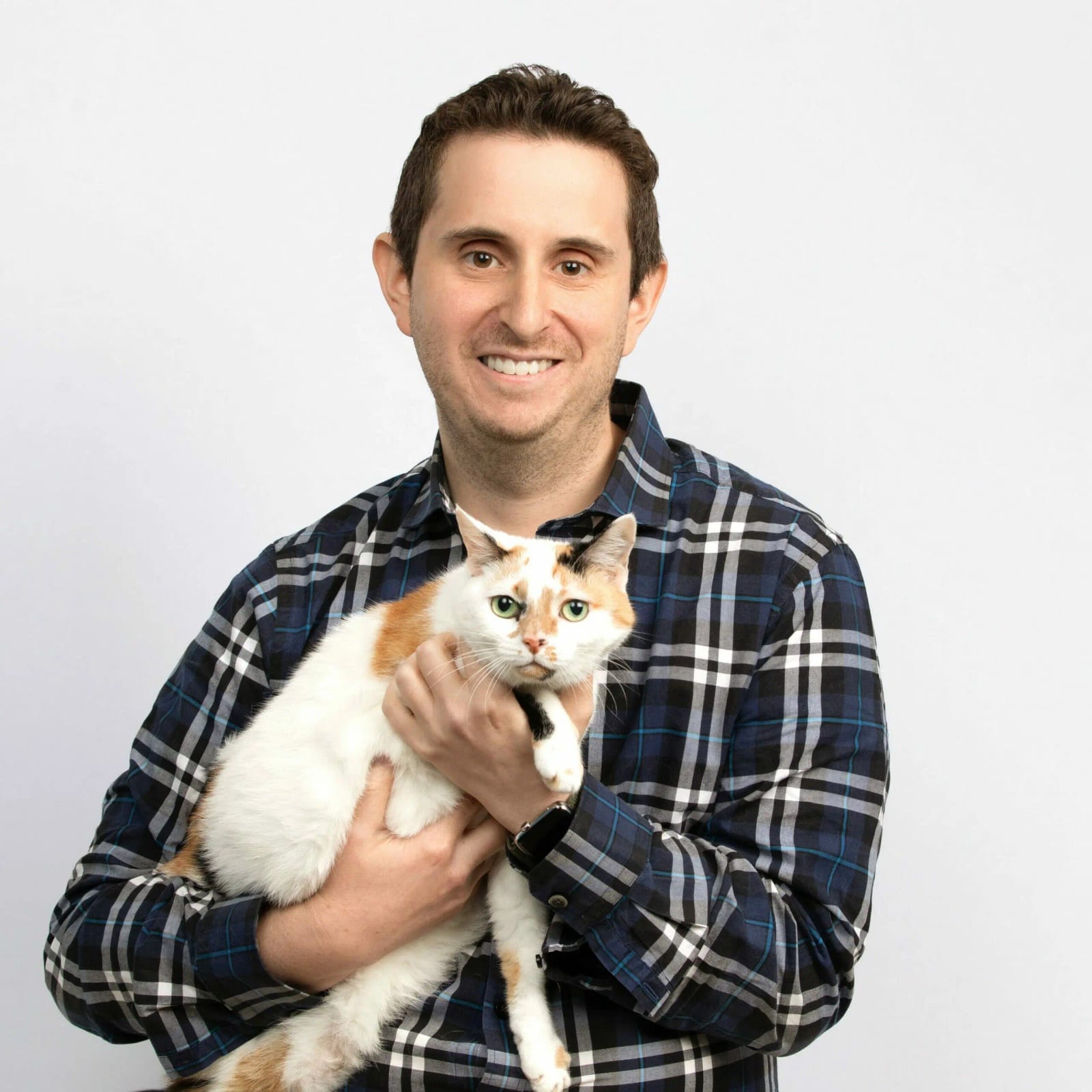 Smiling person in a navy and white plaid shirt holding a white cat with orange patches
