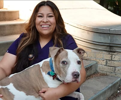 Smiling person in a dark blue top holding a brown and white dog beside stone steps
