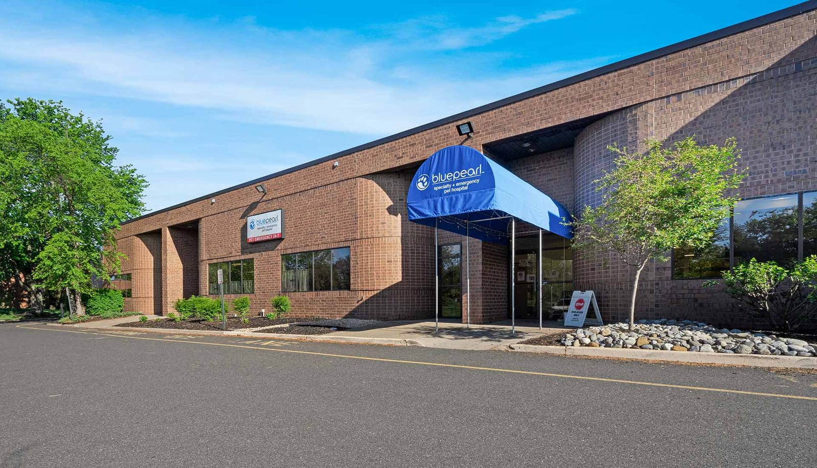BluePearl Pet Hospital brick building with a blue awning, trees and a rock border