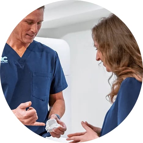 Man and woman in navy scrubs talking, the man holding a small white object in his hand