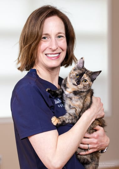 Smiling woman with a brown bob in a navy top holding a tortoiseshell cat