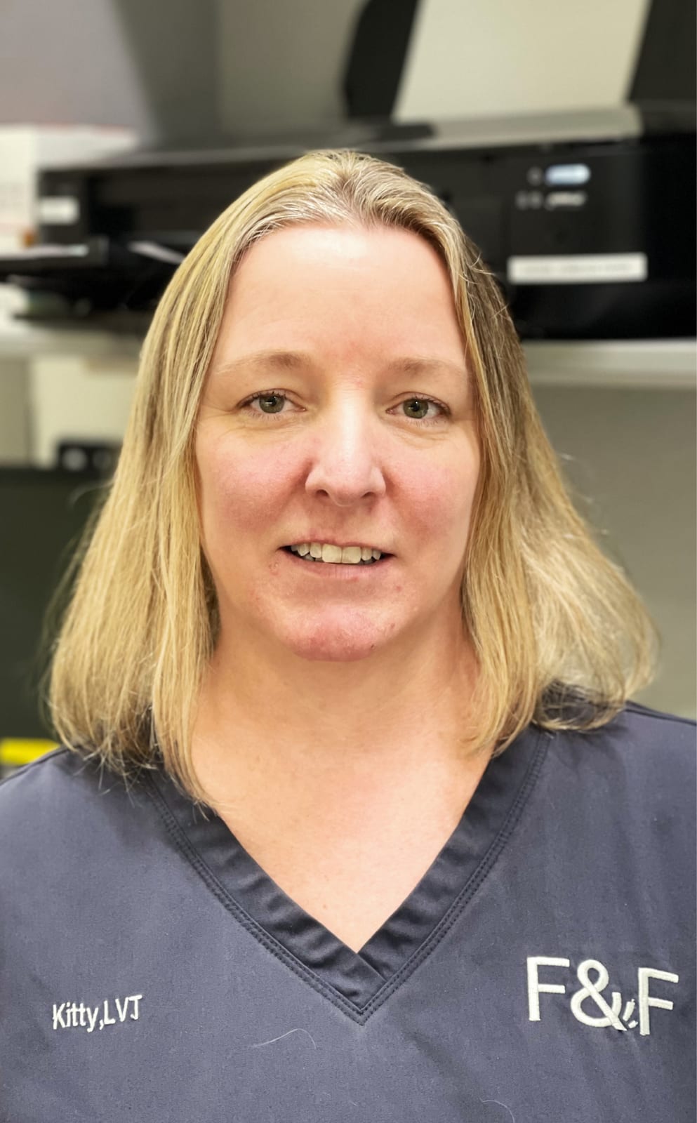 Woman with shoulder-length blond hair wearing navy scrubs marked F&F