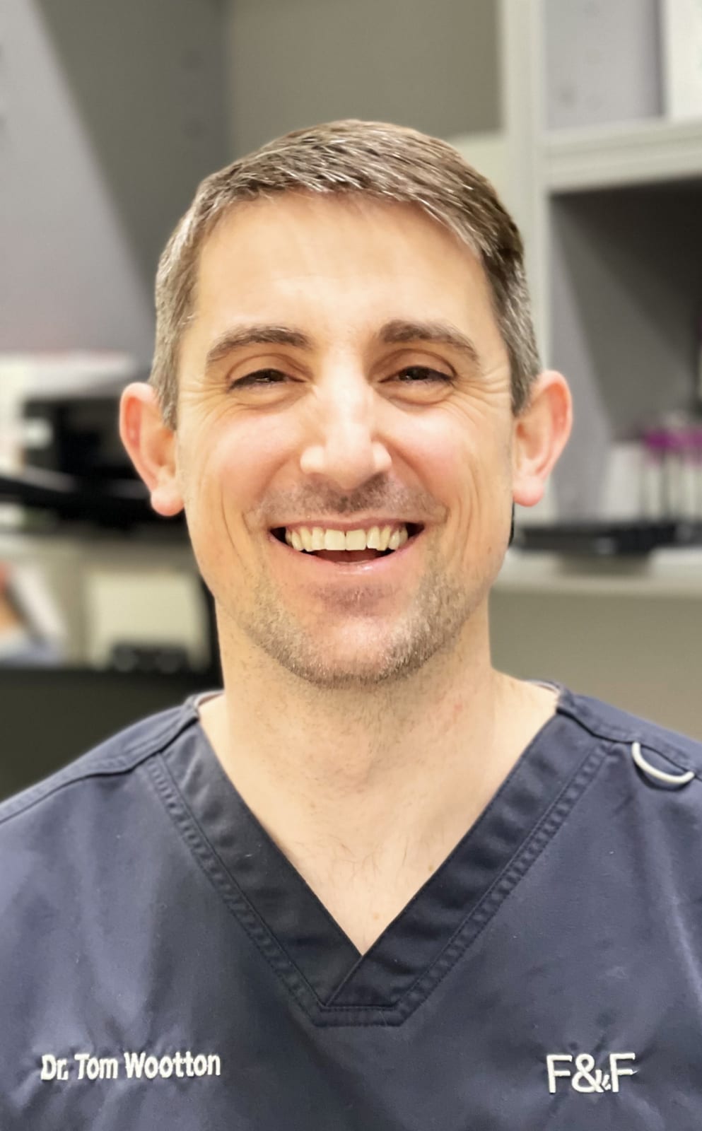 Smiling man with short brown hair wearing navy scrubs marked F&F