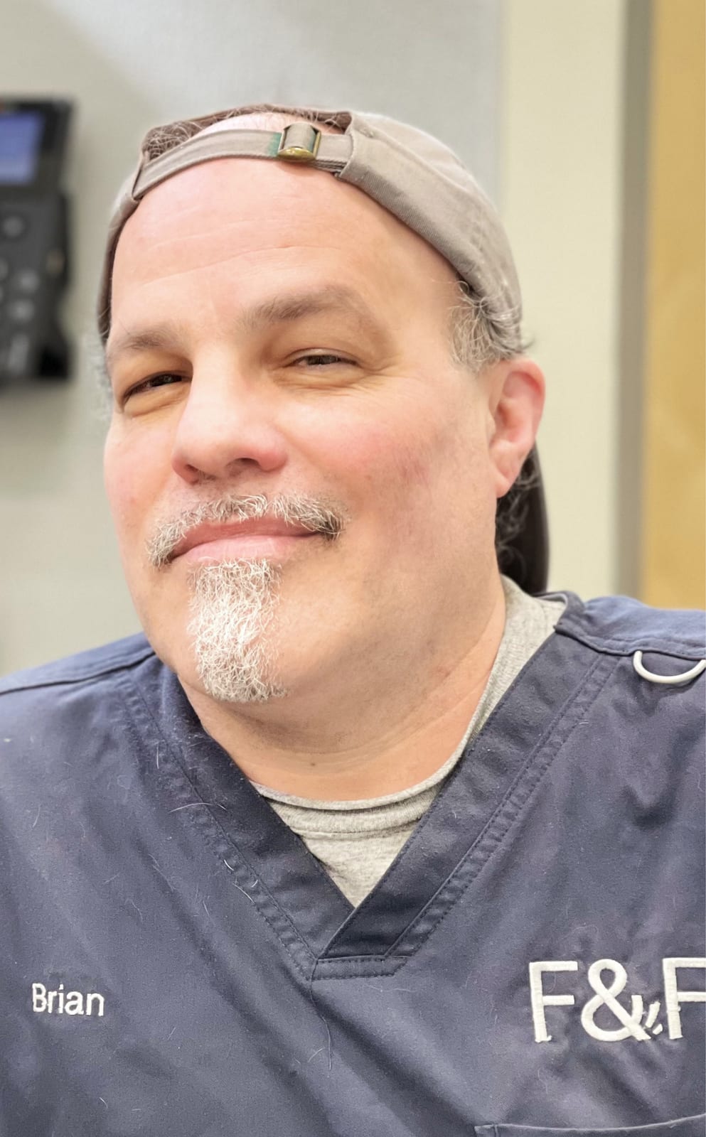 Smiling man in a backwards grey cap and navy scrubs marked F&F