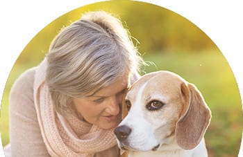 Older woman with grey hair and a pink scarf leaning her head close to a brown and white dog