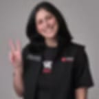 Blurred portrait of a smiling woman with dark hair in a black vest holding up two fingers