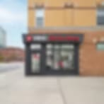 Blurred storefront on a street corner with a dark entrance and a red-lettered sign under a brick upper floor
