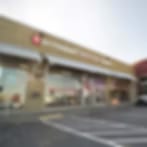Small blurry photo of a storefront with a red logo on its sign, beside a parking lot