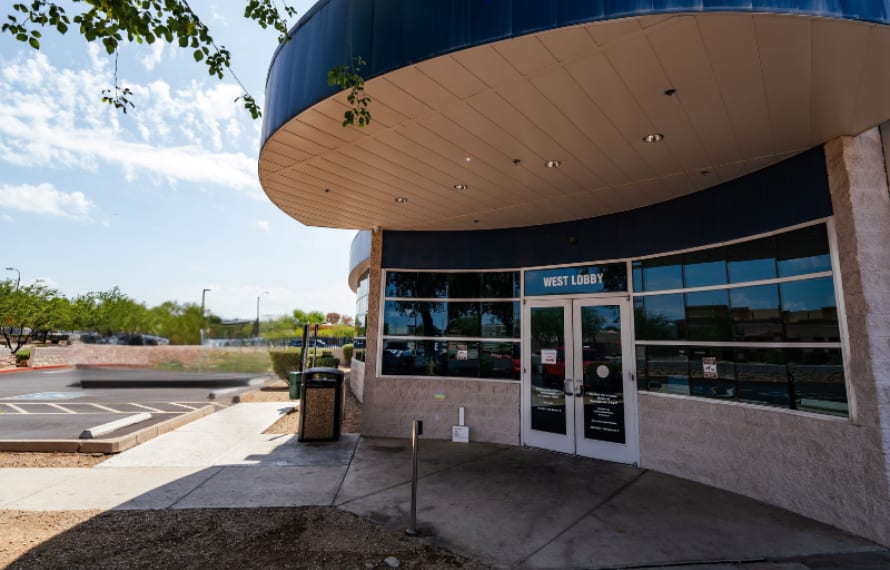 Curved building entrance with a blue roof edge and a West Lobby sign above glass doors