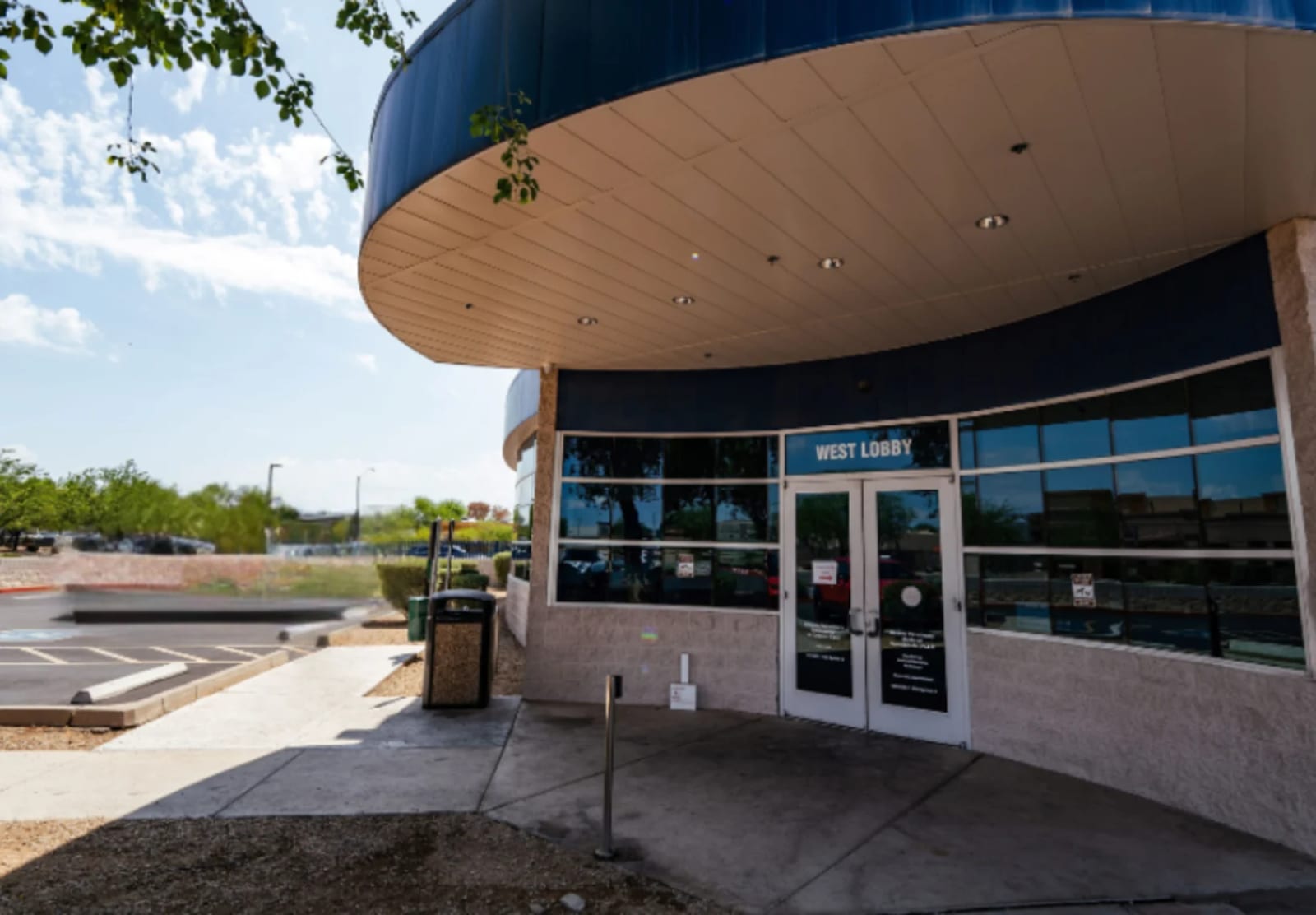 Curved building entrance with a blue roof edge and a West Lobby sign above glass doors