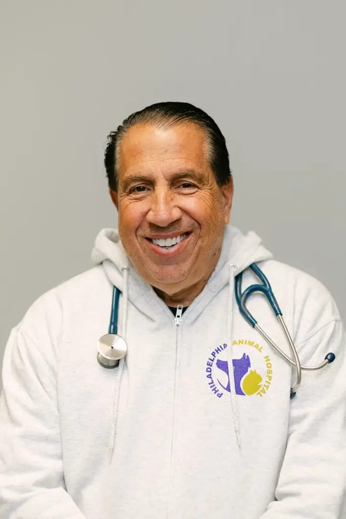 Smiling man in a white hooded sweatshirt with a Philadelphia Animal Hospital logo and a stethoscope around his neck