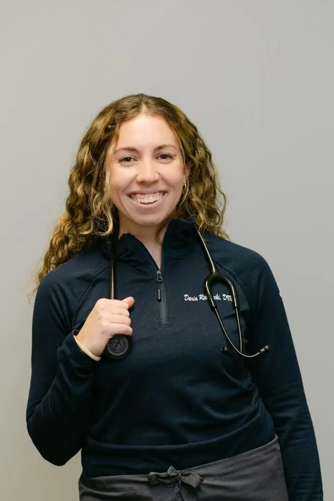 Smiling woman with long curly hair in a navy zip top with a stethoscope around her neck