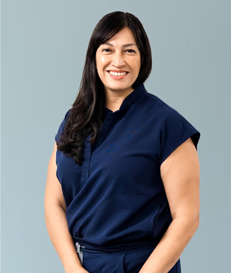 Smiling woman with long dark hair and bangs in a navy top, hands clasped in front of her