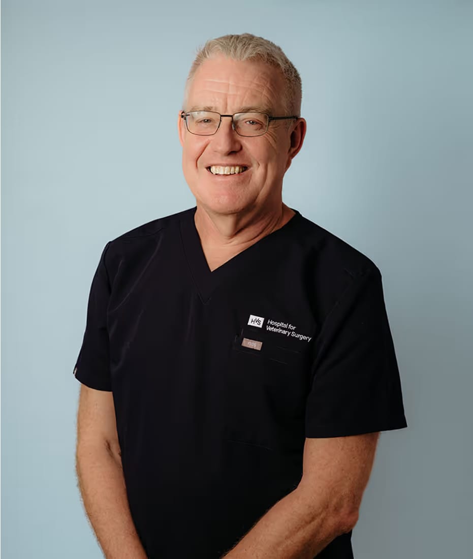 Smiling man with grey hair and glasses in black scrubs with a logo, against a pale blue background
