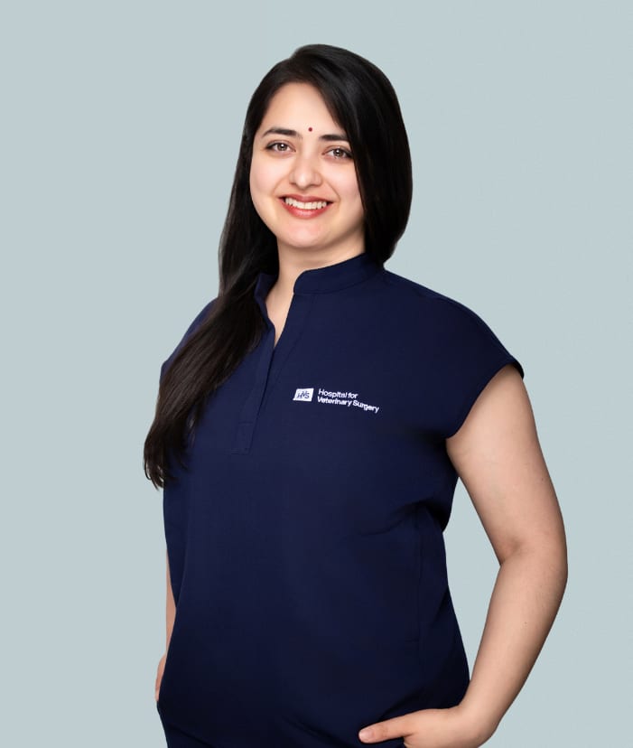 Smiling woman with long dark hair in a navy scrub top with a logo, against a pale grey-blue background