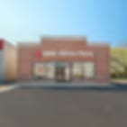 Small blurry image of a low tan building with a sign above glass doors under a blue sky