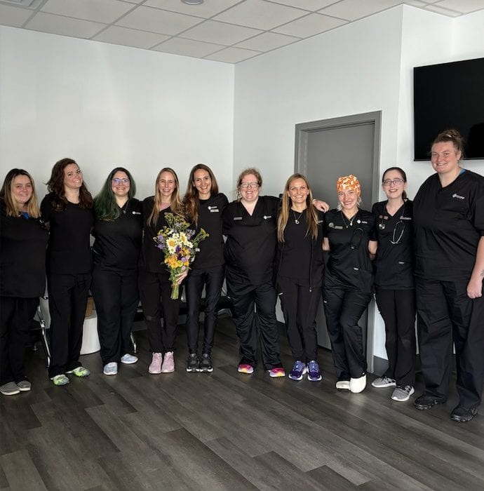 Group of people in black scrubs standing in a row in a room, one holding a bouquet of flowers