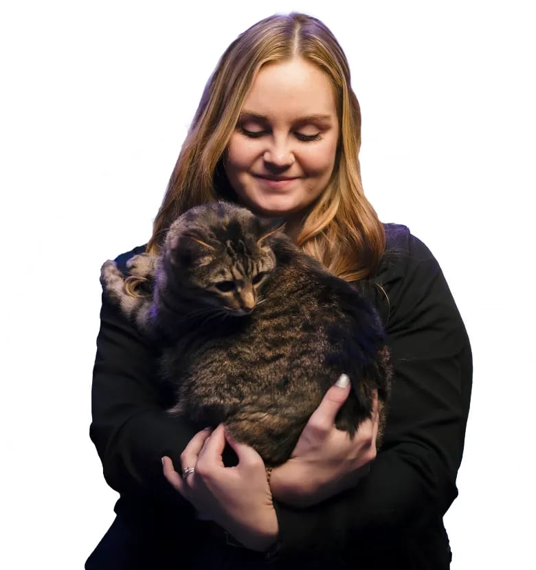 Smiling person with long hair in a black top cradling a brown tabby cat, cut out on white