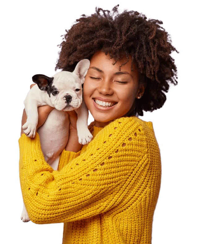 Smiling person in a yellow knit sweater hugging a small white puppy with black ears