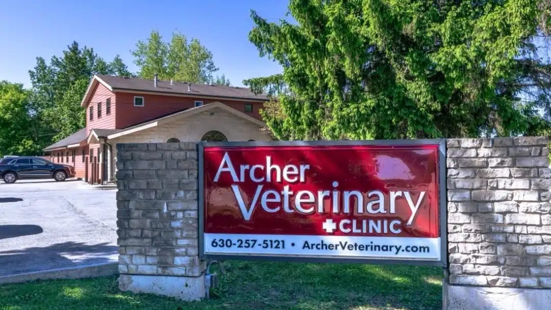 Red Archer Veterinary Clinic sign on stone pillars in front of a brick and wood building