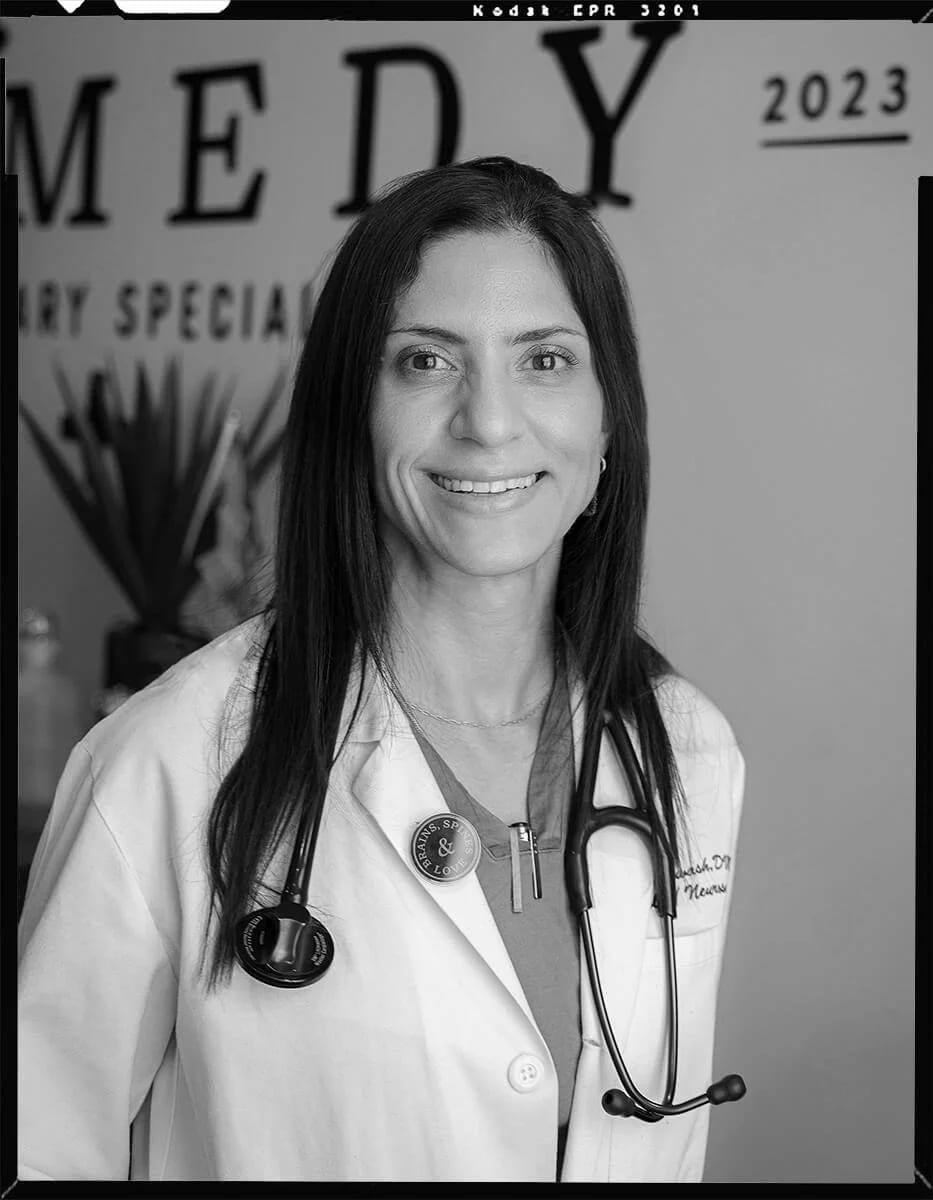 Black and white portrait of a smiling woman in a white coat with a stethoscope and a round pin