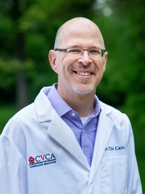 Smiling man with glasses in a white coat with a CVCA logo standing in front of trees