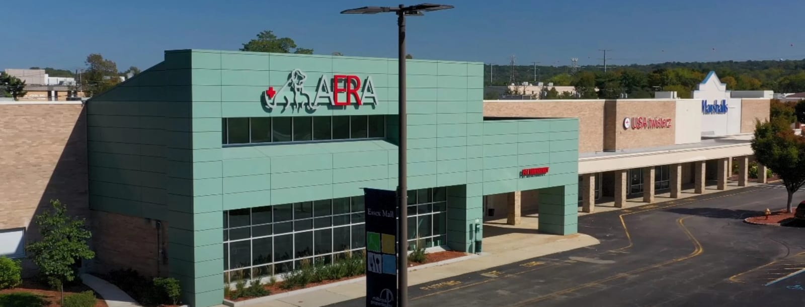 Wide view of a teal-green building with an AERA sign next to a shopping plaza