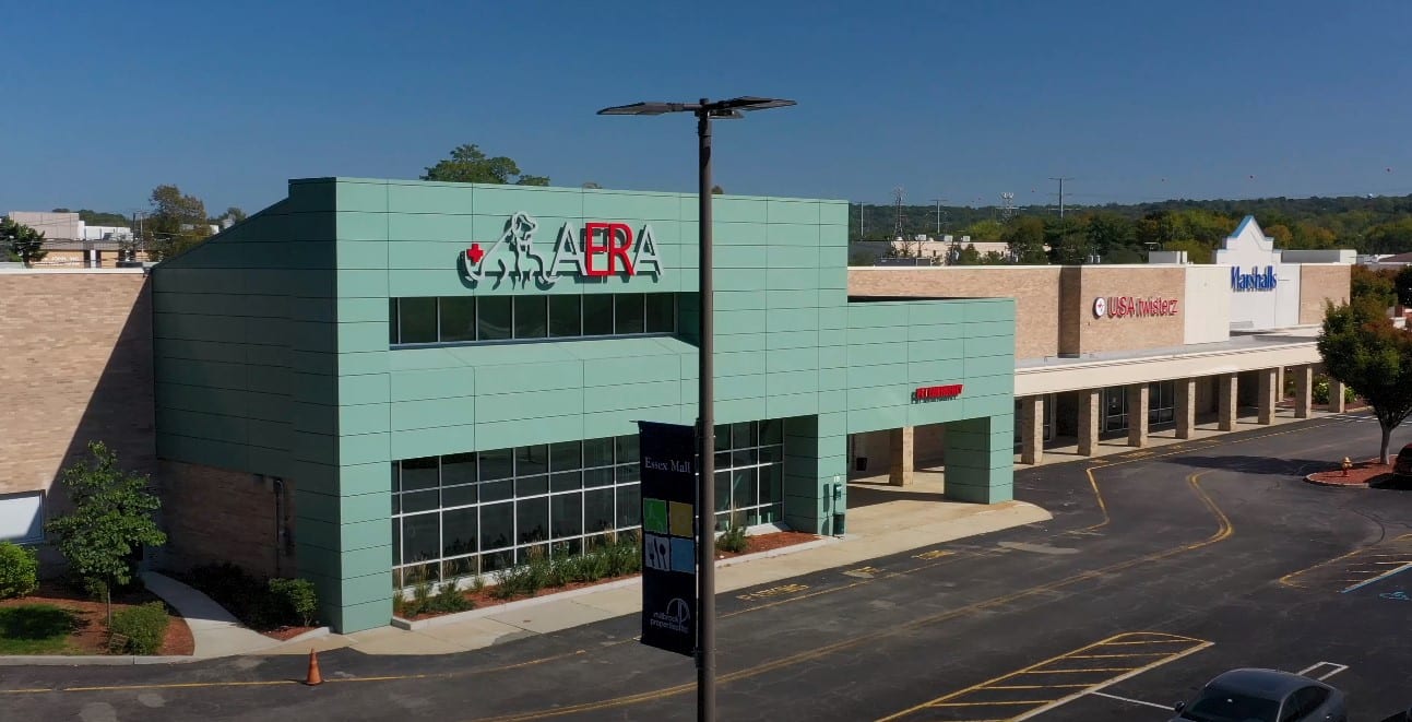 Teal-green building with an AERA sign beside a shopping plaza and a parking lot