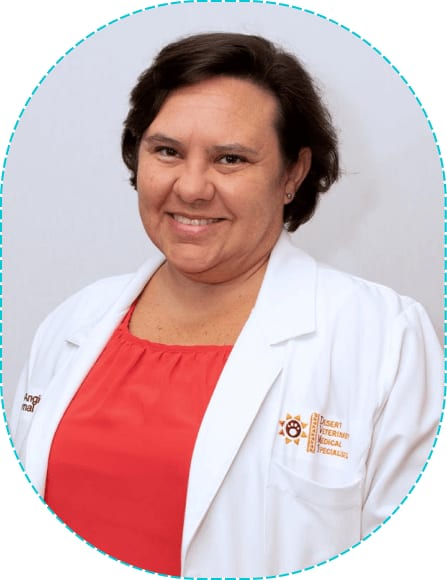Smiling woman with short dark hair in a coral top under a white coat in an oval frame