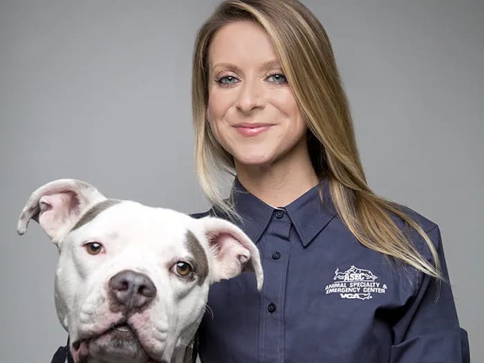 Smiling woman with long blonde hair in a navy shirt beside a white dog with brown eye patches