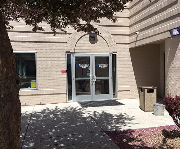 Glass double doors with a blue logo on a tan brick building with an arched entrance