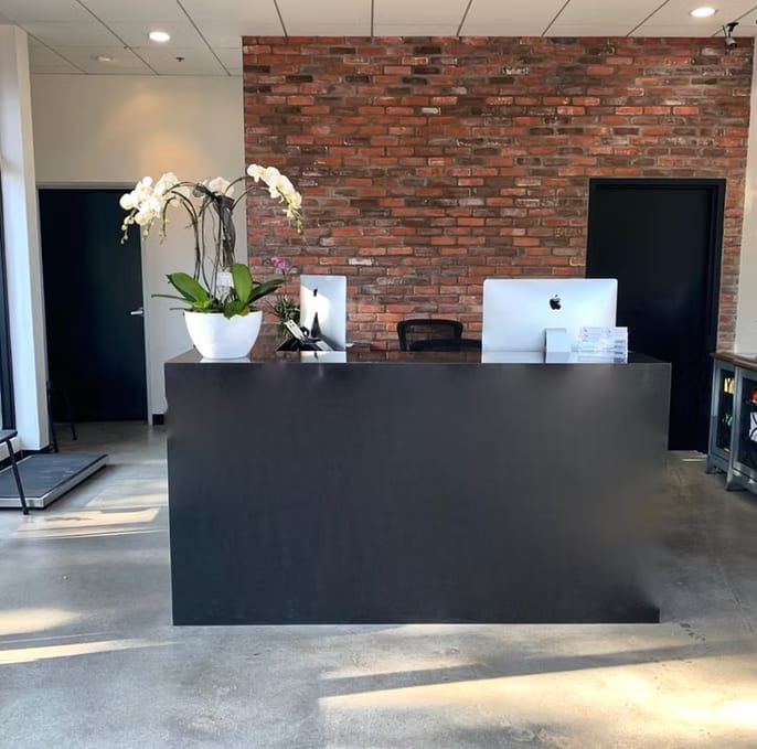 Black reception desk with a white orchid and computers in front of a red brick wall