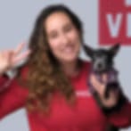Very small blurry image of a smiling woman in a red top holding a small dark dog and making a peace sign