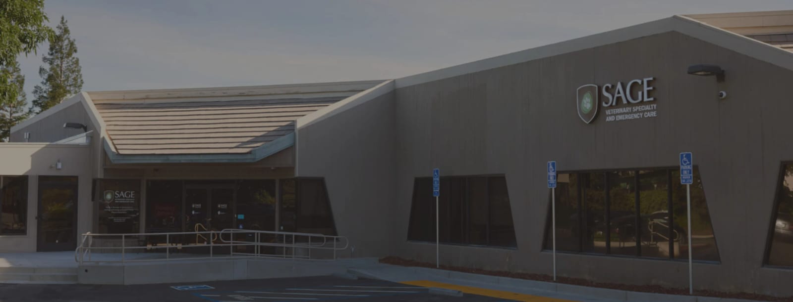 SAGE building with a tiled roof section, grey wall, shield logo and accessible parking signs in front