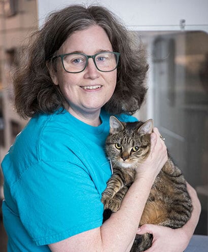 Smiling person with glasses and a teal T-shirt holding a tabby cat
