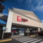 Heavily blurred image of a tan building with a red sign against a blue sky