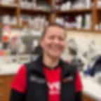 Low-resolution photo of a smiling person in a red shirt and dark vest in front of shelves