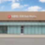Heavily blurred image of a low tan building with a teal glass front and a red sign