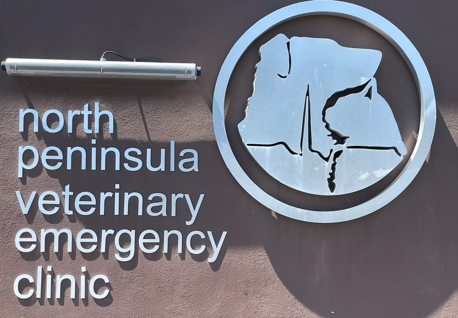 North Peninsula Veterinary Emergency Clinic sign with a circular dog and heartbeat emblem on a brown wall