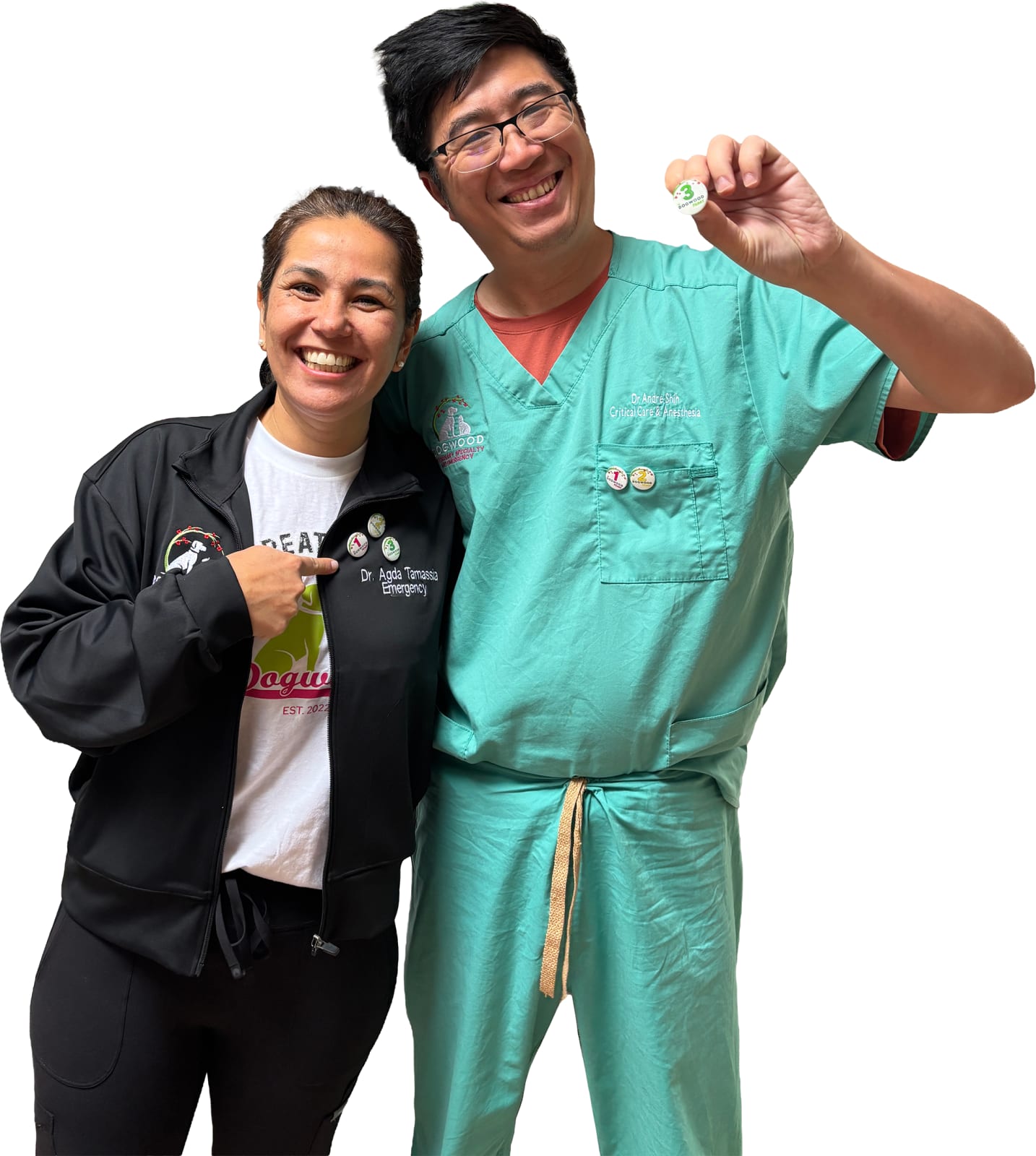Two smiling people, one in teal scrubs holding up a small pin and one in a black jacket