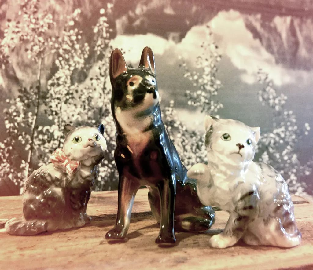 Three ceramic figurines, a dog in the middle and a cat on each side, on a wooden surface