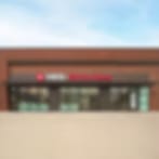 Blurry low-resolution image of a brick-red building with a dark awning and glass front under a blue sky