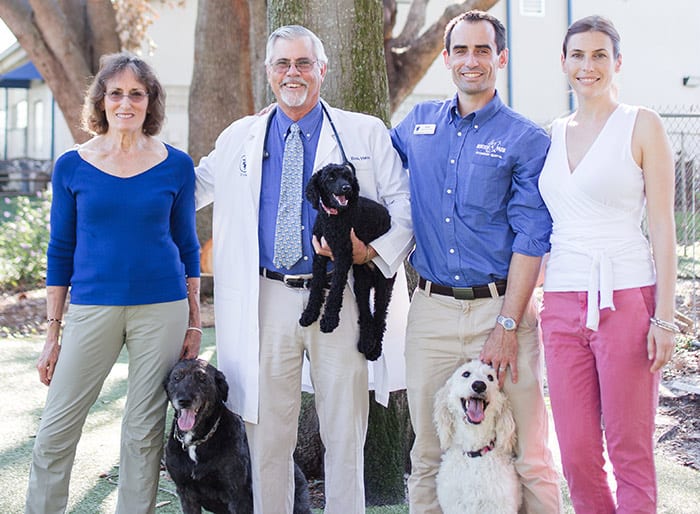 Four adults standing outdoors with three dogs, one man holding a small black puppy