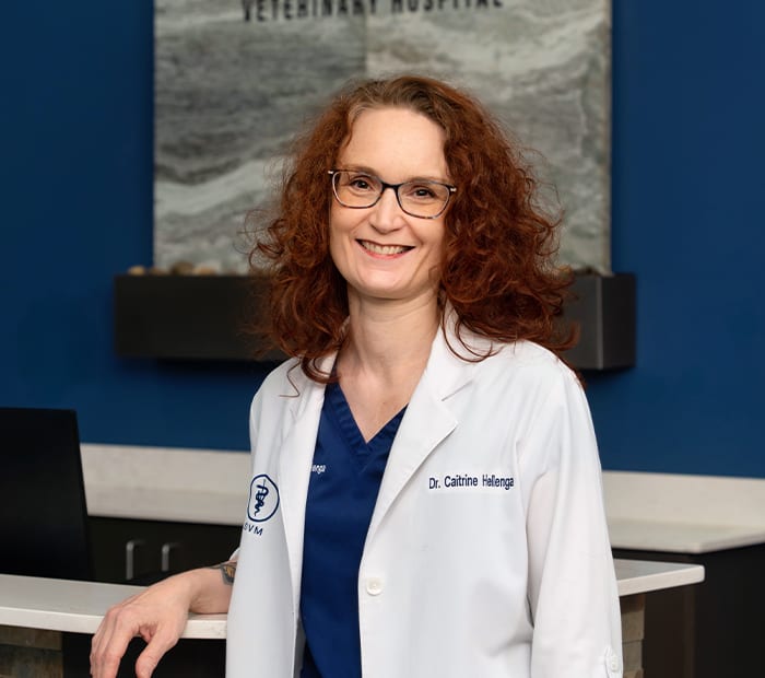 Smiling woman with curly red hair and glasses in a white coat over navy scrubs