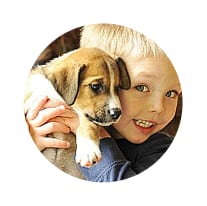 Child with light hair hugging a brown and white puppy, shown in a circular crop