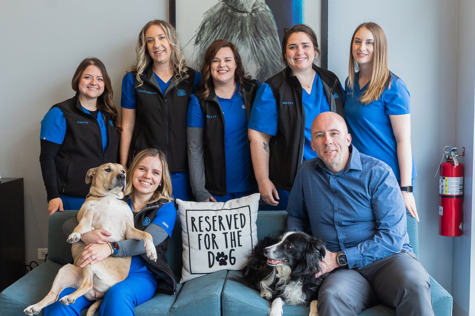 Seven people and two dogs on a teal couch with a pillow reading Reserved for the dog