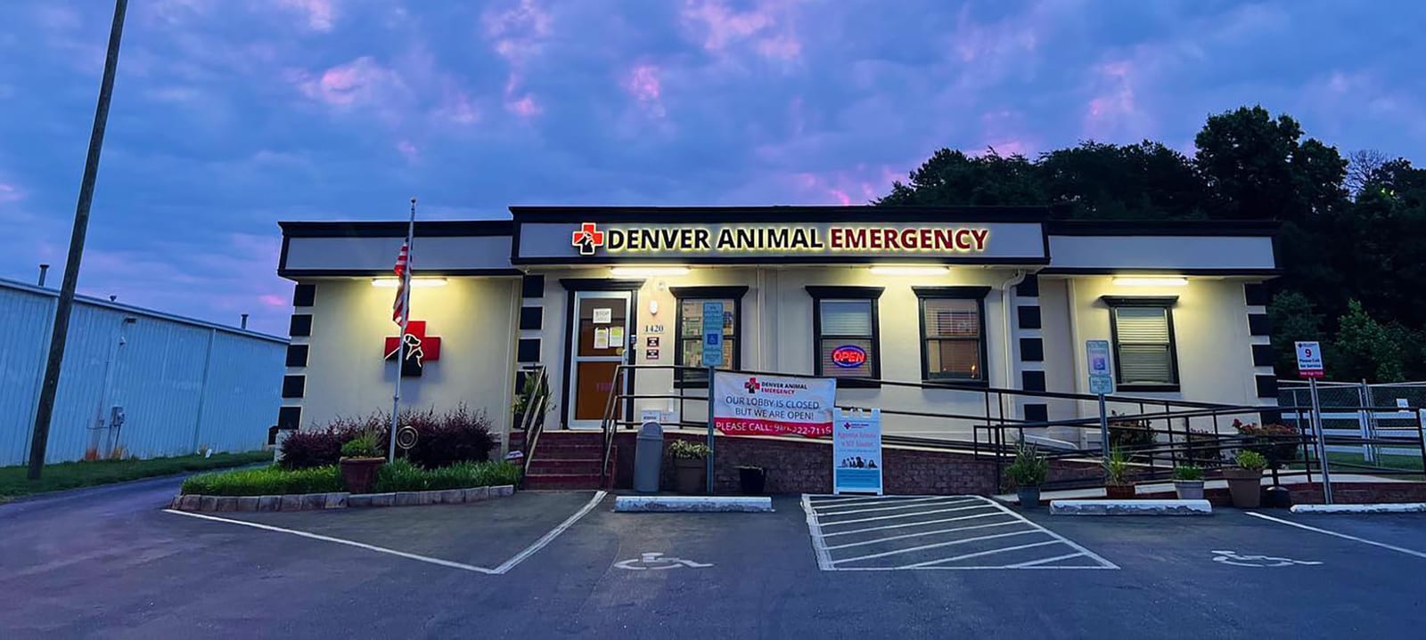 Denver Animal Emergency building at dusk with a lit sign, a red cross logo and a parking lot