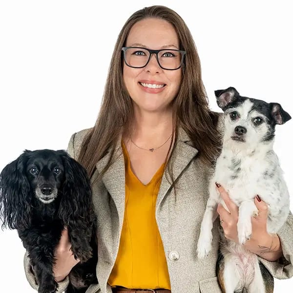 Smiling woman in glasses holding two small dogs, one black and one white with black patches