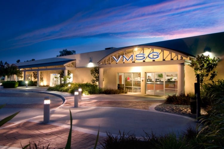 Building entrance at dusk with a lit VMSG sign, curved driveway and landscaped bollard lights