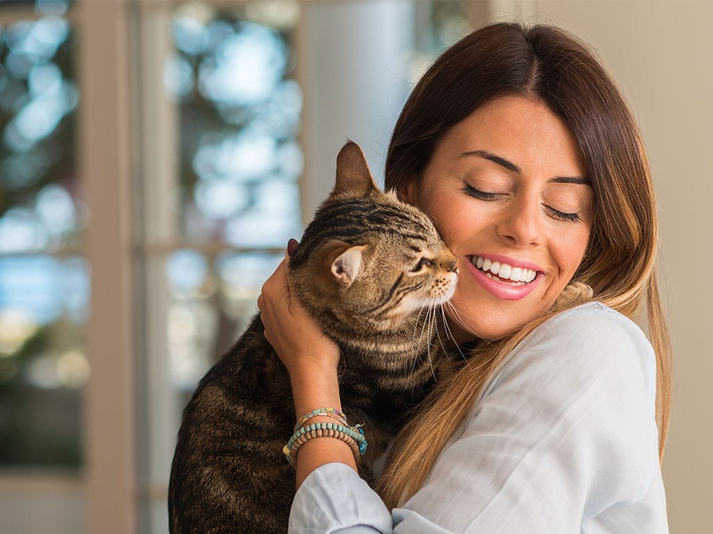 Smiling woman hugging a brown tabby cat in a bright room